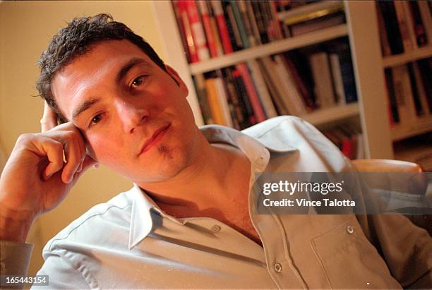 Pics of Evan Solomon sitting with bookcase that he built in back and light from his standing lamp shines upon his face.Nice and mmody.