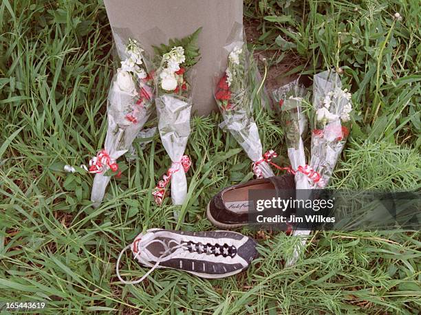 Five identical flower bouquets and two shoes lie in grass at the base of a railway barrier support where five men died when the minivan they were in...