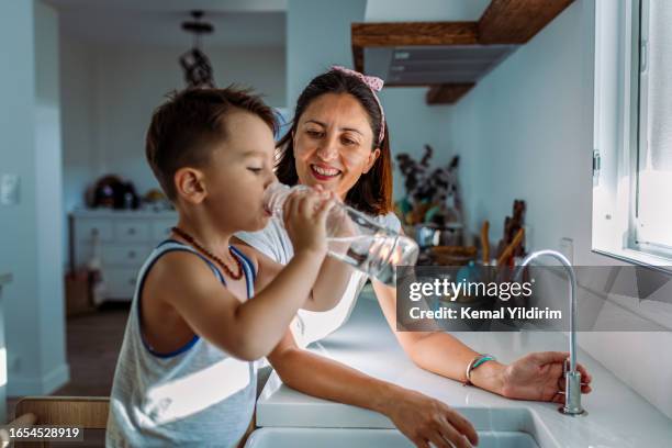 mutter und ihr kleinkind füllen ein glas mit gefiltertem wasser direkt aus dem wasserhahn - trinkwasser stock-fotos und bilder
