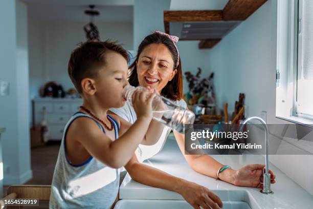 mother and her toddler filling a glass with filtered water right from the tap - fluor stockfoto's en -beelden