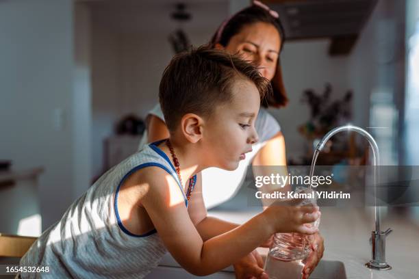 madre y su niño pequeño llenando un vaso con agua filtrada directamente del grifo - niño-tomando-agua fotografías e imágenes de stock