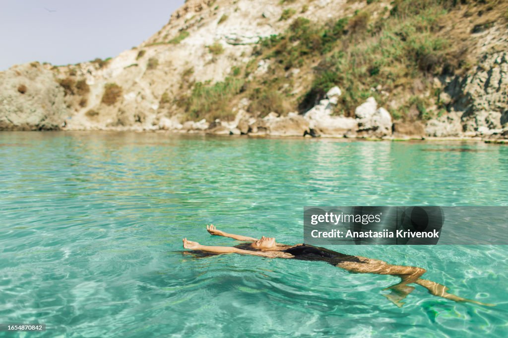 Beautiful multiracial woman in black swimsuit with long hair enjoying clear transparent ocean.