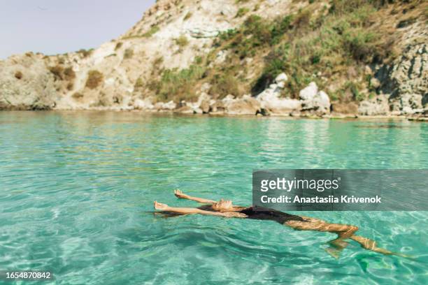 beautiful multiracial woman in black swimsuit with long hair enjoying clear transparent ocean. - cyprus stockfoto's en -beelden