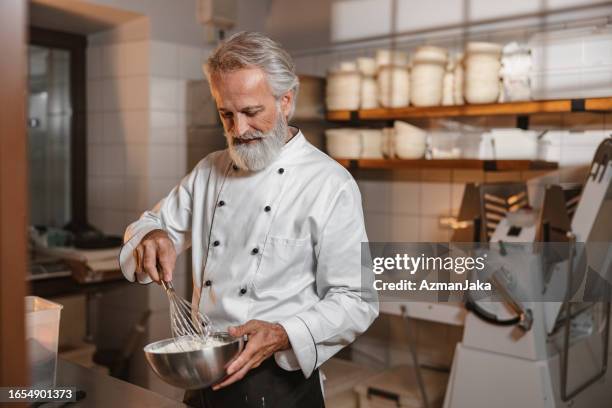 caucasian baker mixing a dough with a hand whisk in the kitchen - baker smelling bread stockfoto's en -beelden