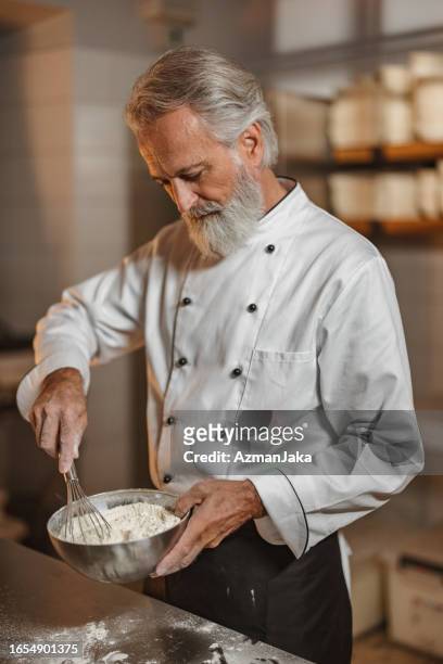 boulanger expérimenté mélangeant une pâte pour le pain dans la cuisine de la boulangerie - baker smelling bread photos et images de collection