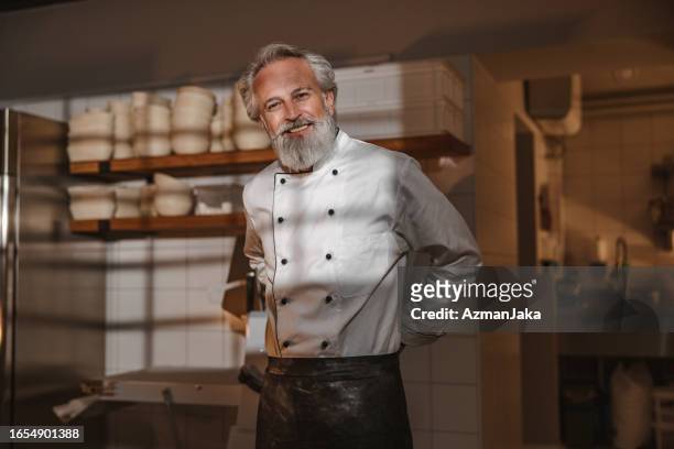 smiley mature baker getting ready to start working at sunrise - baker smelling bread stockfoto's en -beelden