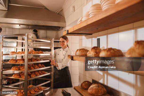 panadera caucásica empujando un carrito de bandeja para hornear lleno de croissants - panadería fotografías e imágenes de stock