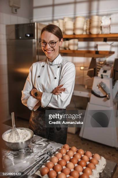 caucasian female baker smiling with arms crossed in the bakery - baker smelling bread stockfoto's en -beelden