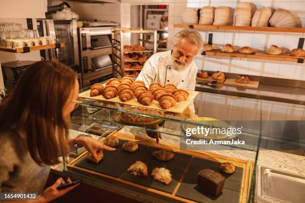 caucasian baker attending a young female costumer at the bakery - baker smelling bread stockfoto's en -beelden