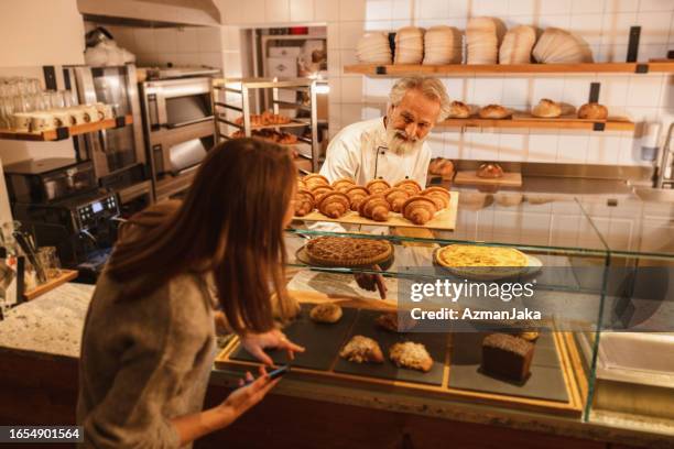 caucasian baker attending a young female costumer at the bakery - baker smelling bread stock pictures, royalty-free photos & images