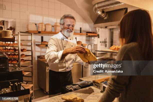 caucasian baker packing an order for a young costumer at the bakery - baker smelling bread stockfoto's en -beelden