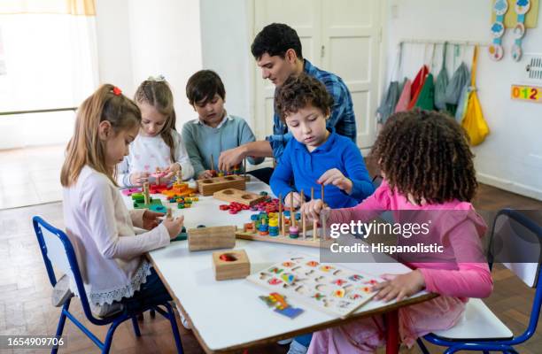 diverse group of kids at school playing with wooden toys while male teacher supervises and interacts with them - child care worker stock pictures, royalty-free photos & images