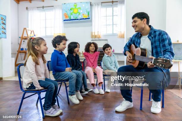 diverse group of 7 year olds at school having fun in music class with male cheerful teacher - child care worker stockfoto's en -beelden