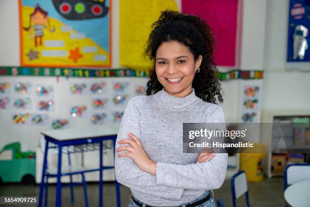 portrait of confident cheerful female elementary school teacher smiling at the camera with arms crossed - child care worker stock pictures, royalty-free photos & images