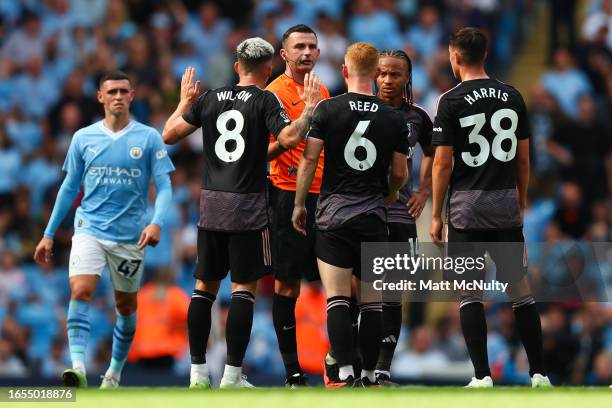 Referee Michael Oliver explains a decision to Harry Wilson and Harrison Reed of Fulham after awarding Manchester City a 3rd goal after a VAR review...