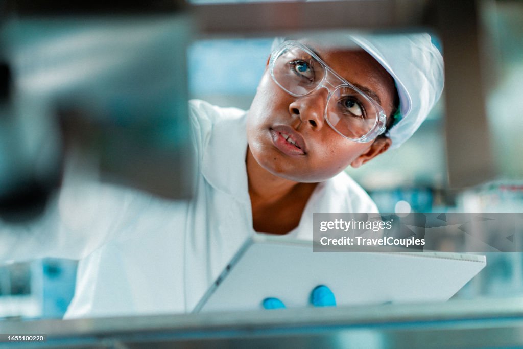 Female engineer in a drinking water factory in professional uniform using digital tablet working in beverage industrial. Female factory worker use digital tablet testing program in production line.