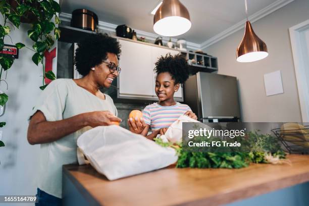 mother and daughter talking and unpacking fruits and vegetables in the kitchen at apartment - superfood stock pictures, royalty-free photos & images