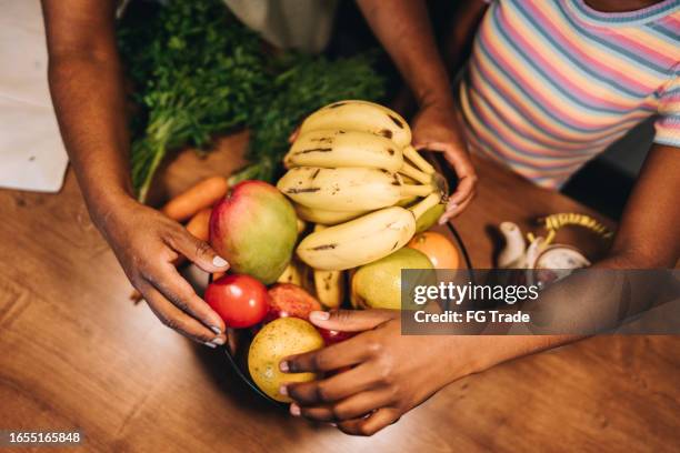 close-up of mother and daughter hands putting fruits on fruit bowl in the kitchen at home - fruitschaal stockfoto's en -beelden