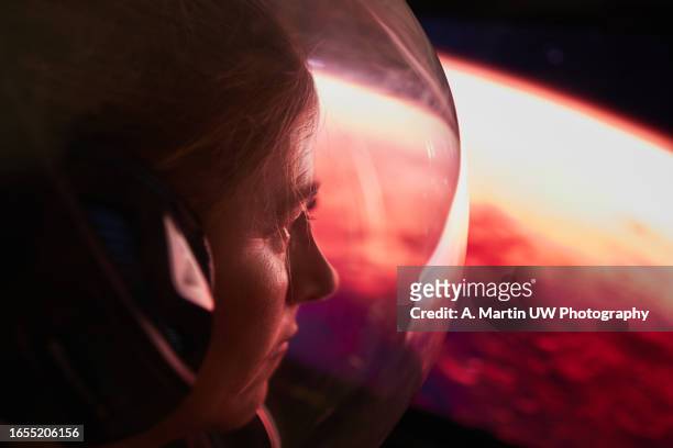 female astronaut wearing a space helmet and looking to mars through the space shuttle window. space journey concept. - launch of cinematic pictures publishings men of science fiction arrivals stockfoto's en -beelden
