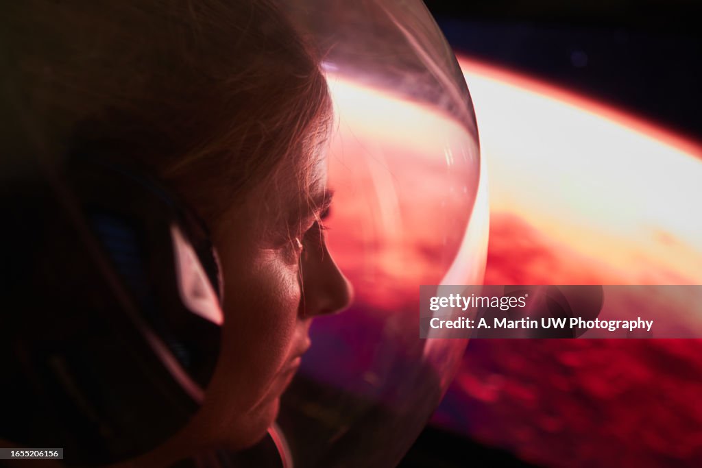 Female astronaut wearing a space helmet and looking to Mars through the space shuttle window. Space journey concept.