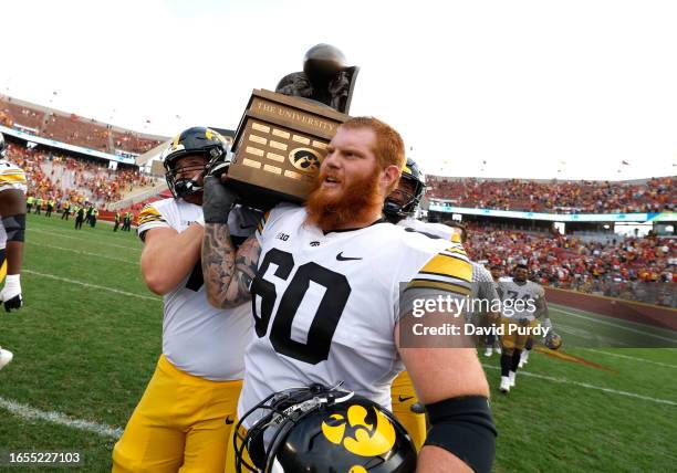 Offensive lineman Tyler Elsbury and offensive lineman Rusty Feth of the Iowa Hawkeyes carry the Cy-Hawk Trophy off the field after winning 20-13 over...