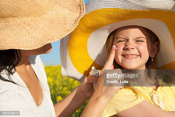 mother rubbing sunscreen on daughter - sun hat stock pictures, royalty-free photos & images