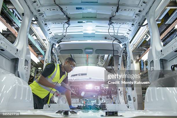 Car worker wearing high visibility jacket fitting parts on vehicle on production line in car factory