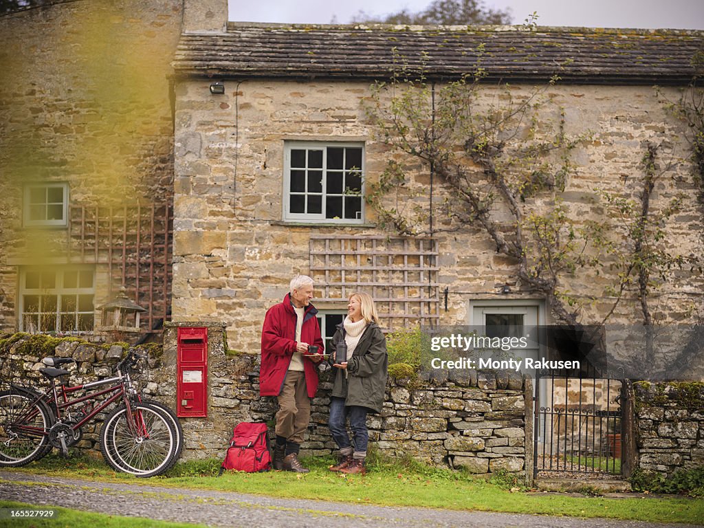 Couple with bicycles standing by dry stone wall and cottage in rural village