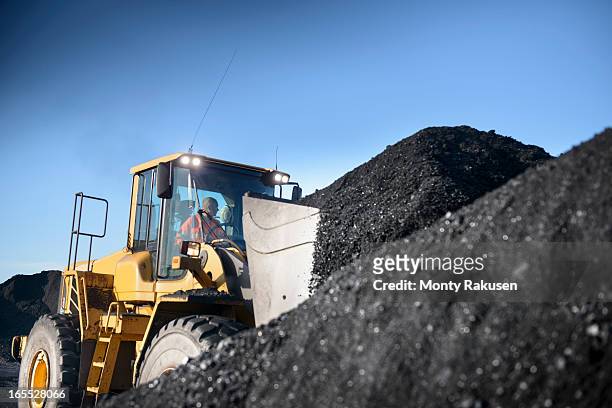 worker operating digger with pile of coal at surface coal mine - coal mine stock photos et images de collection