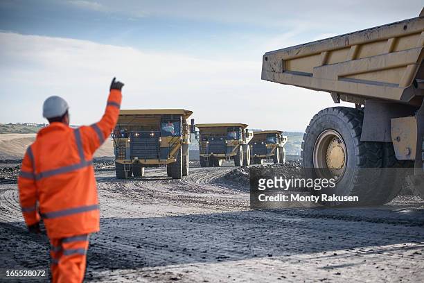 worker waving on dumpers driving on track at surface coal mine - mining worker stock pictures, royalty-free photos & images