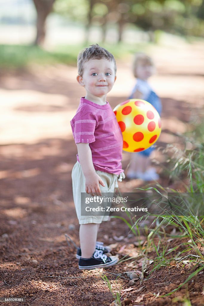 Toddler boy with ball on dirt road