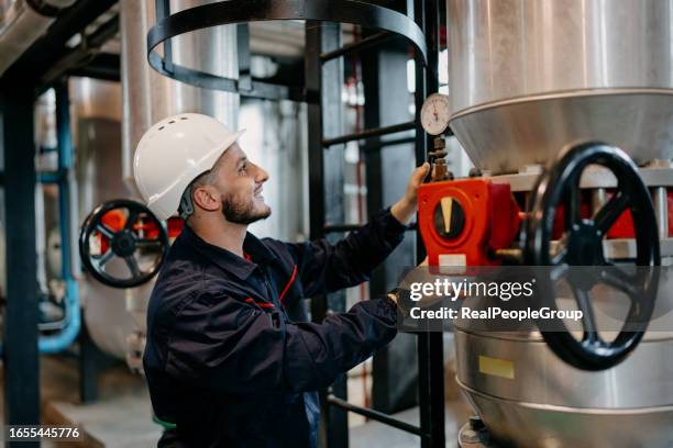 ein junger kaukasischer ingenieur mit schutzhelm dreht das rad an einem rohrsystem. - district heating stock-fotos und bilder