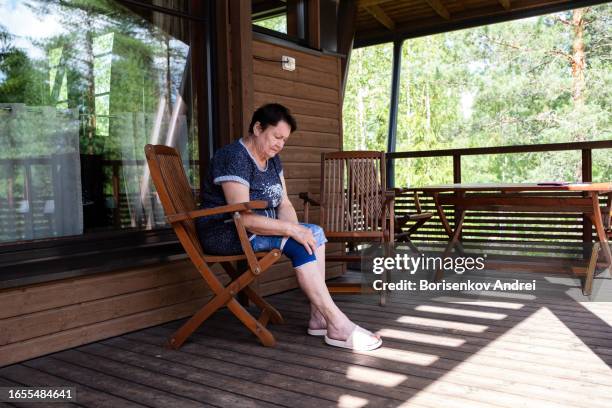 una anciana, de 78 años, masajea su rodilla dolorida. la mujer tiene un vendaje elástico, sufre de reumatismo - articulación humana fotografías e imágenes de stock