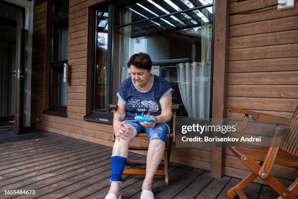 una anciana, de 78 años, se pone crema en la rodilla. mujer que sufre de reumatismo - articulación humana fotografías e imágenes de stock