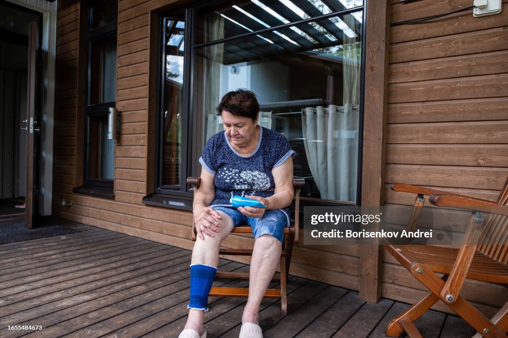 An elderly woman, 78 years old, puts cream on her knee. Woman suffering from rheumatism