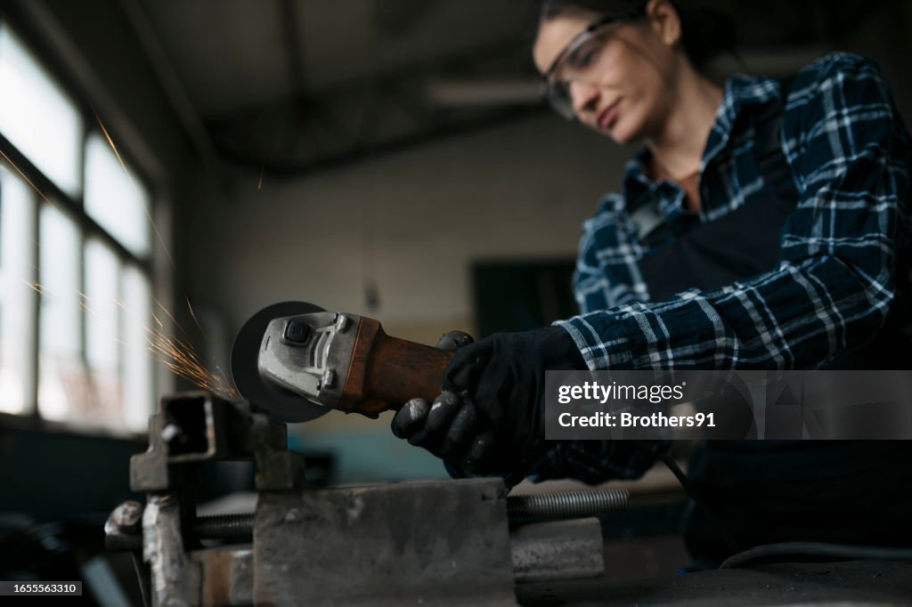 Woman working in industrial workshop grinding a metal piece with an angle grinder