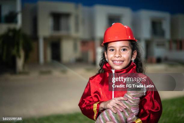 portrait of a child girl with a firefighter costume holding a toy cat outdoors - boy fireman costume stock pictures, royalty-free photos & images