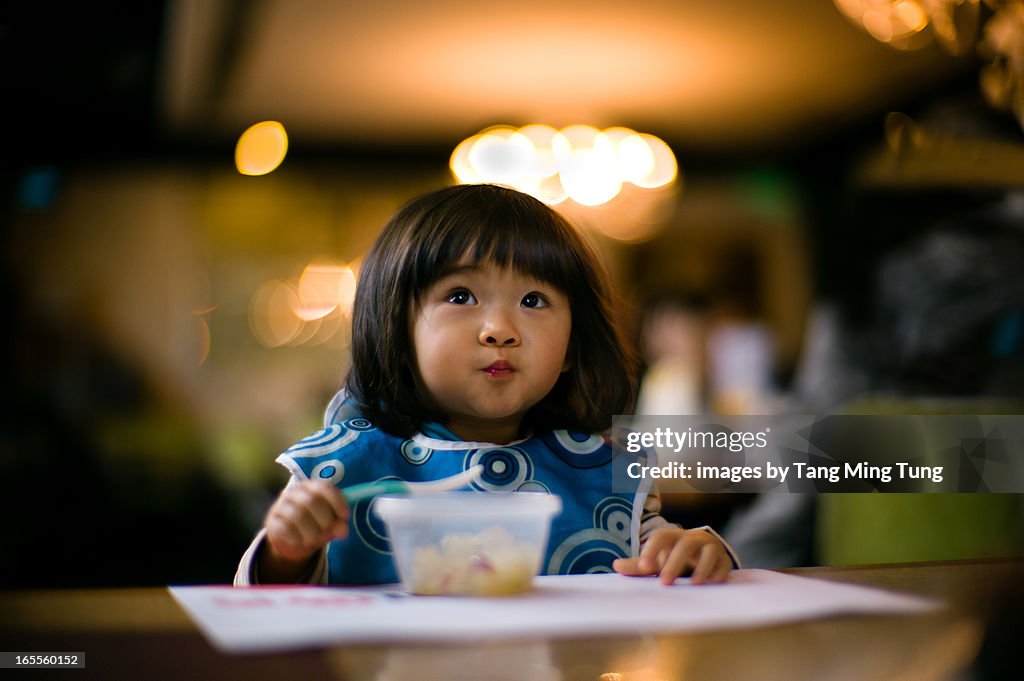 Thoughtful toddler girl feeding herself with spoon