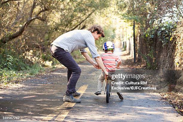 father teaching son to ride bicycle - father helping son wearing helmet stock pictures, royalty-free photos & images