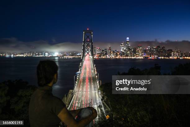 Woman watches the city and San Francisco-Oakland Bay Bridge view during cloudy weather at night in Treasure Island of San Francisco, California,...