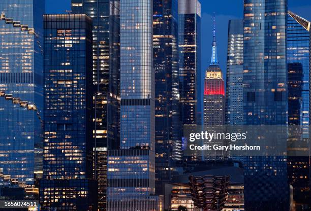 The Empire State Building lit in red, white, and blue to mark Labor Day weekend stands between the towers of Hudson Yards as the sun sets in New York...