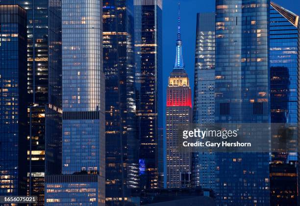 The Empire State Building lit in red, white, and blue to mark Labor Day weekend stands between the towers of Hudson Yards as the sun sets in New York...