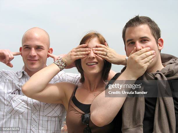 Portrait of one woman and two men who simulate the three wise monkeys by covering the eyes, the ears and the mouth. The young guys want to...