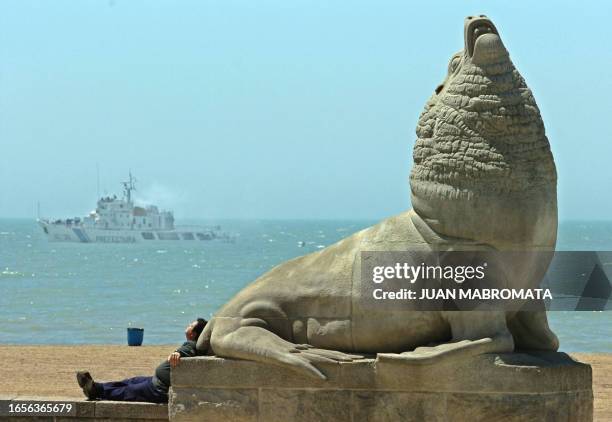 Mar del Plata inhabitant takes a sun bath lying down on one of the typical Mar del Plata sea lions with a coastguard vessel in the background, 05...