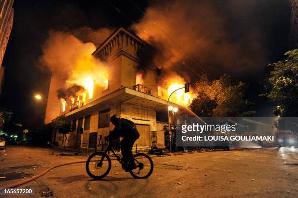Man rides his bicycle pas a burning building in Athens during massive clashes on February 12, 2012. Greek police fired tear gas at petrol...