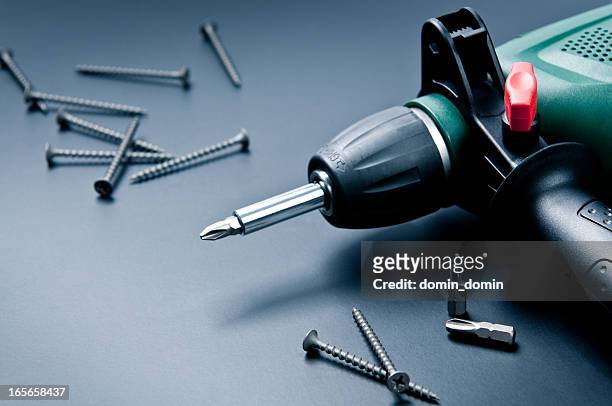 electric drill with screws and screwdrivers on dark background - elektrisch gereedschap stockfoto's en -beelden