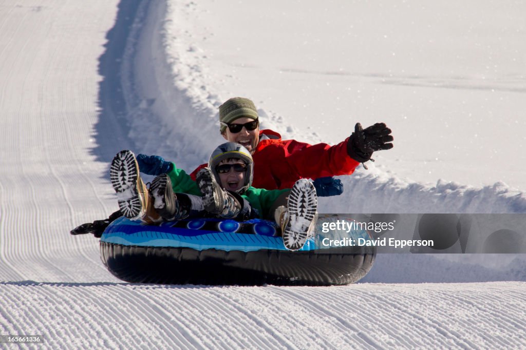 Father and son snow tubing on groomed path