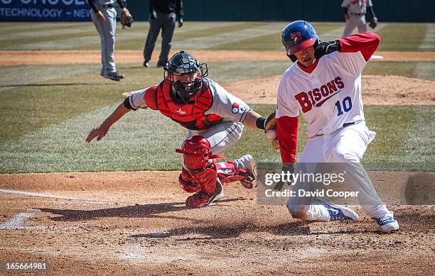 Bisons Ryan Goins slides in safe at home ahead of the tag of Red Wings catcher Chris Herrmann during opening day for the Blue Jays new AAA farm team...