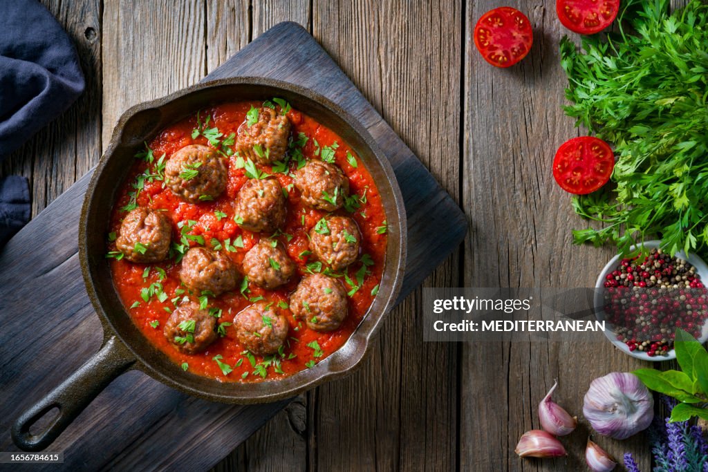 Meat balls with tomato sauce homemade in rustic cast iron pan over wood