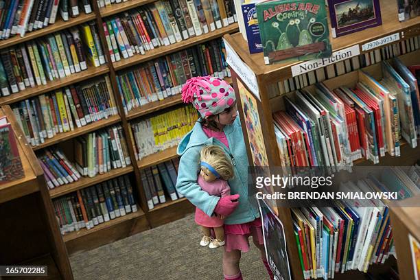 Girl holds an American Girl doll while looking at books in the Cherrydale Branch of the Arlington Library April 4, 2013 in Arlington, Virginia. The...